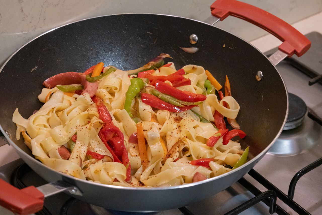 our-services-05 Delicious pasta mixed with vibrant vegetables in a frying pan on the stove.