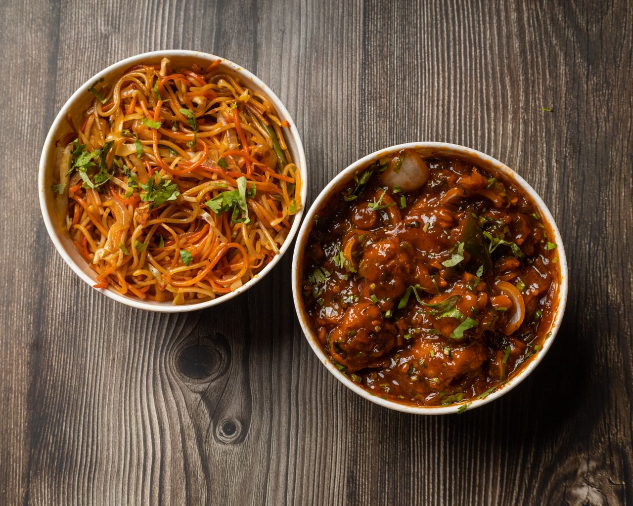 about-img Vibrant bowls of Indo-Chinese noodles and Manchurian on a rustic wooden surface.