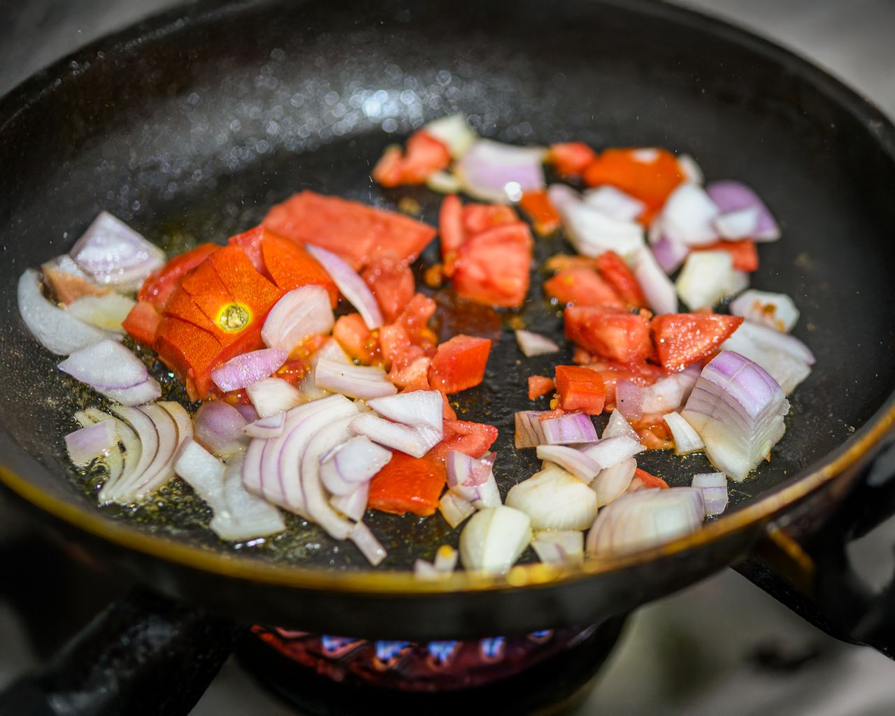 hero-gallery-01 Close-up of tomatoes and onions being sautéed in a frying pan over a stove.